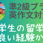「準2級プラス英作文対策」と書かれたタイトルとともに、「中学生の留学は良い経験か？」という日本語の問いが白抜き文字で表示されたバナー画像。左側には、アメリカの学校の前で本を持つ日本人中学生のイラストが描かれている。背景は青から緑へのグラデーション。